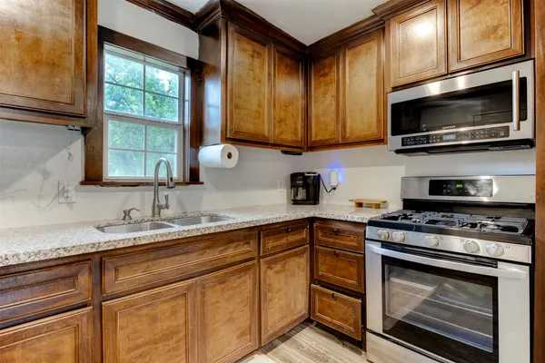 a kitchen with stainless steel appliances granite countertop a sink a stove a microwave and wooden cabinets