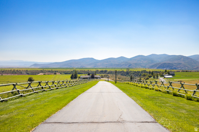 6117 North Rocky Ridge Road Peoa, UT 84061 - Photo 2 of 82 Paved private driveway with split-rail fencing, bordered by manicured lawns and expansive green fields