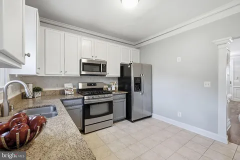 a kitchen with stainless steel appliances granite countertop a stove a sink and a refrigerator with white cabinets