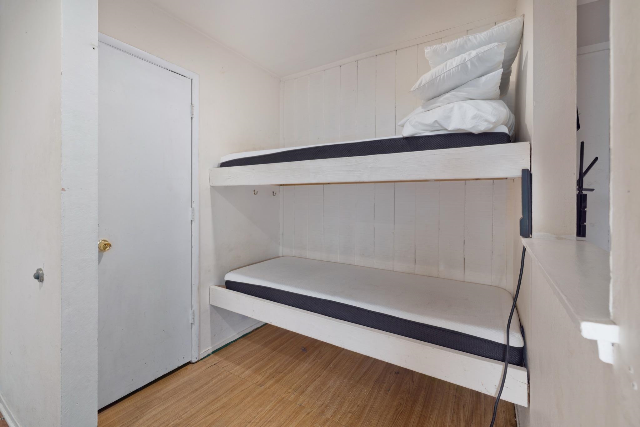 25 Lee Road, Unit 103 Mammoth Lakes, CA 93546 - Photo 21 of 29 Compact sleeping area featuring built-in bunk beds, wood-finish flooring, white painted walls, and a solid white door with a brass-finish knob