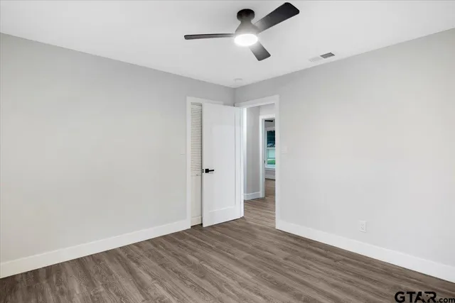 an empty room with wooden floor ceiling fan and window