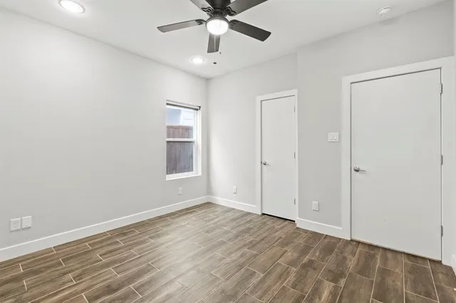 a view of an empty room with wooden floor and a ceiling fan