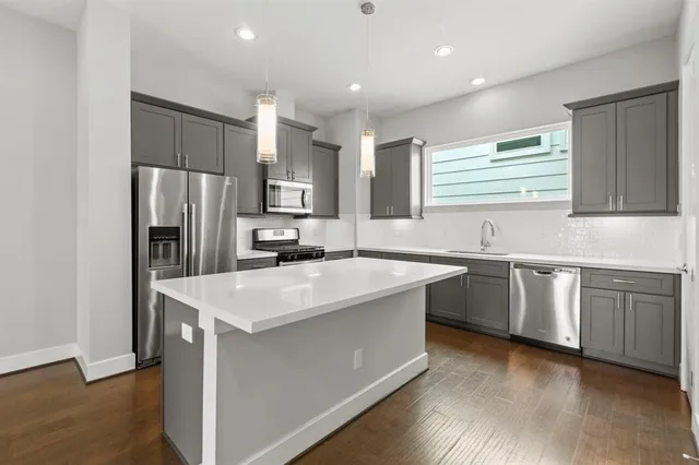 a kitchen with stainless steel appliances granite countertop a sink dishwasher a refrigerator and a stove with wooden floors