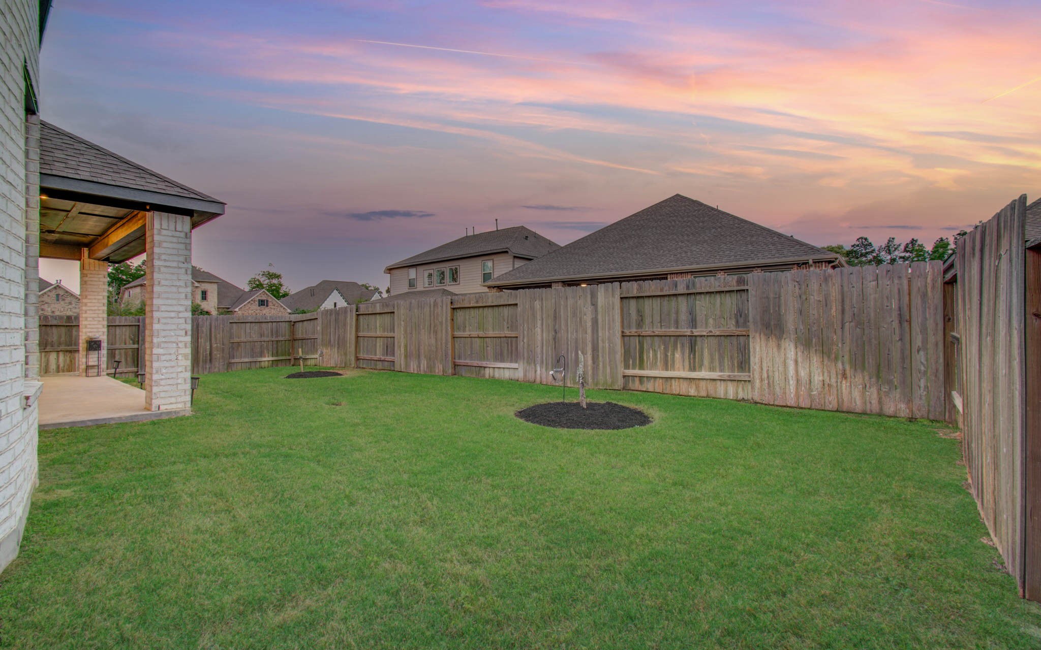 17344 Grand Canyon Road Conroe, TX 77302 - Photo 43 of 49 Spacious backyard with well-maintained lawn and wooden privacy fence, ideal for outdoor activities. The covered patio provides a cozy spot for relaxation, and the sunset view adds a serene ambiance.