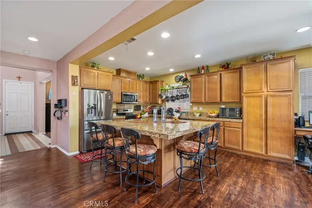 a kitchen with stainless steel appliances kitchen island granite countertop a refrigerator a stove a sink a dining table and chairs with wooden floor