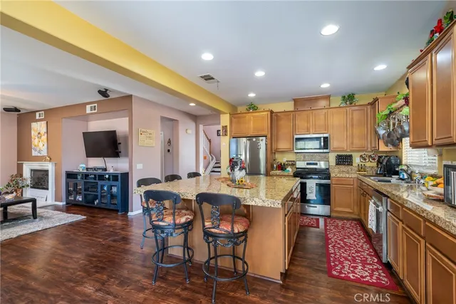 a kitchen with stainless steel appliances kitchen island granite countertop a refrigerator a stove top oven a sink dishwasher a dining table and chairs with wooden floor