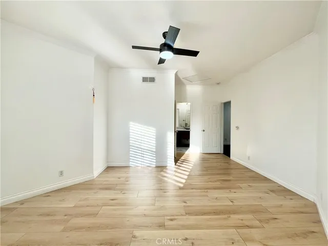 a view of an empty room with wooden floor and a ceiling fan