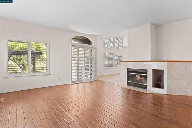 a view of an empty room with wooden floor fireplace and a window