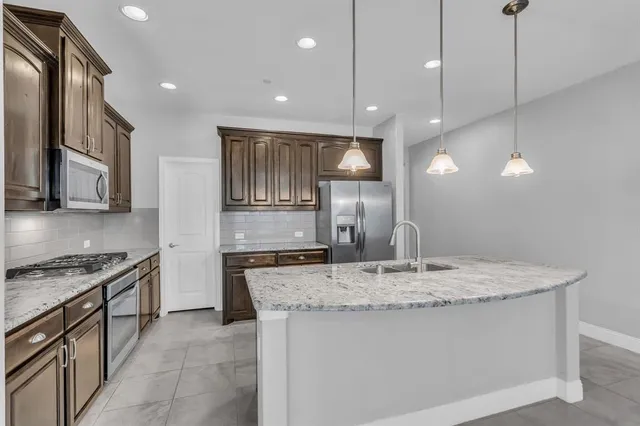 a kitchen with stainless steel appliances granite countertop a refrigerator a stove and a sink with wooden cabinets