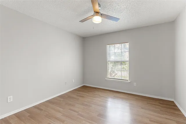 an empty room with wooden floor chandelier fan and windows