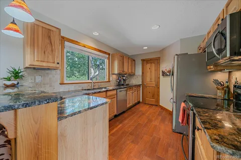 a kitchen with stainless steel appliances granite countertop a refrigerator a stove a sink dishwasher and wooden cabinets with wooden floor