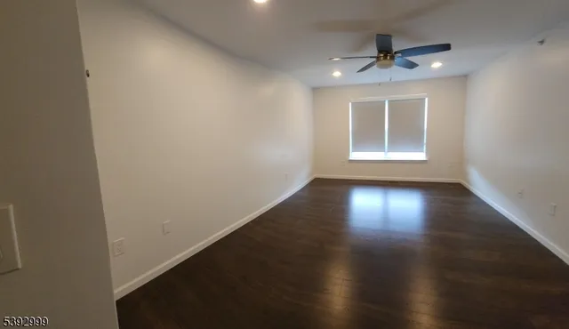 an empty room with wooden floor chandelier fan and windows