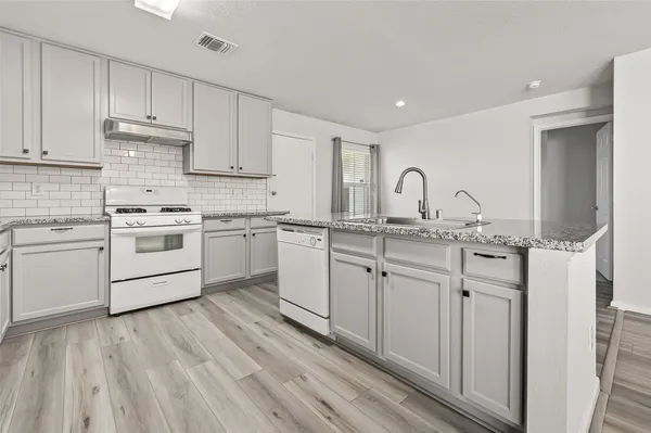 a kitchen with white cabinets stainless steel appliances a sink and a wooden floor