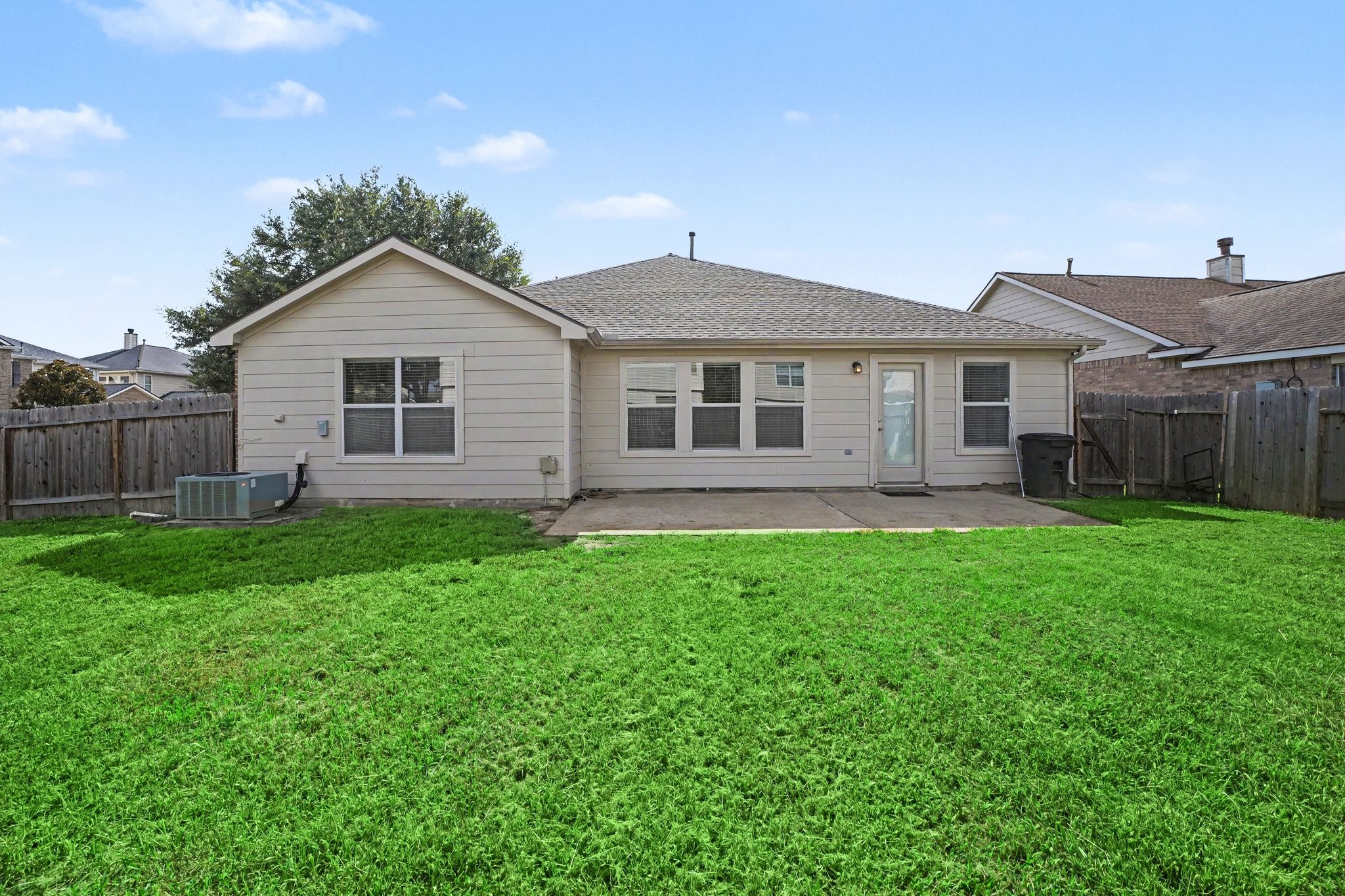 21427 Blooming Rock Lane Spring, TX 77379 - Photo 31 of 32 This photo shows the backyard of a single-story house with beige siding. It features a spacious, fenced yard with a concrete patio area, ideal for outdoor activities and relaxation. The yard is bordered by a wooden fence, providing privacy.