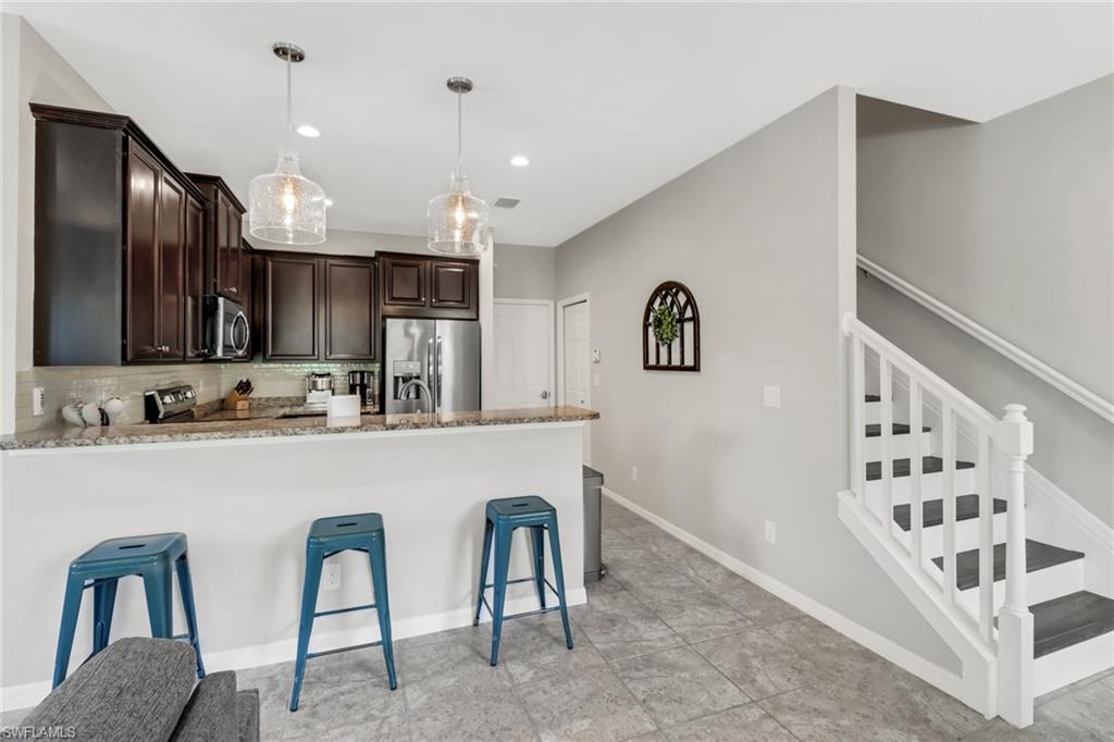 15354 Summit Pl Circle, Unit 159 Naples, FL 34119 - Photo 9 of 27 a kitchen with stainless steel appliances granite countertop a refrigerator a sink dishwasher a dining table and chairs with wooden floor