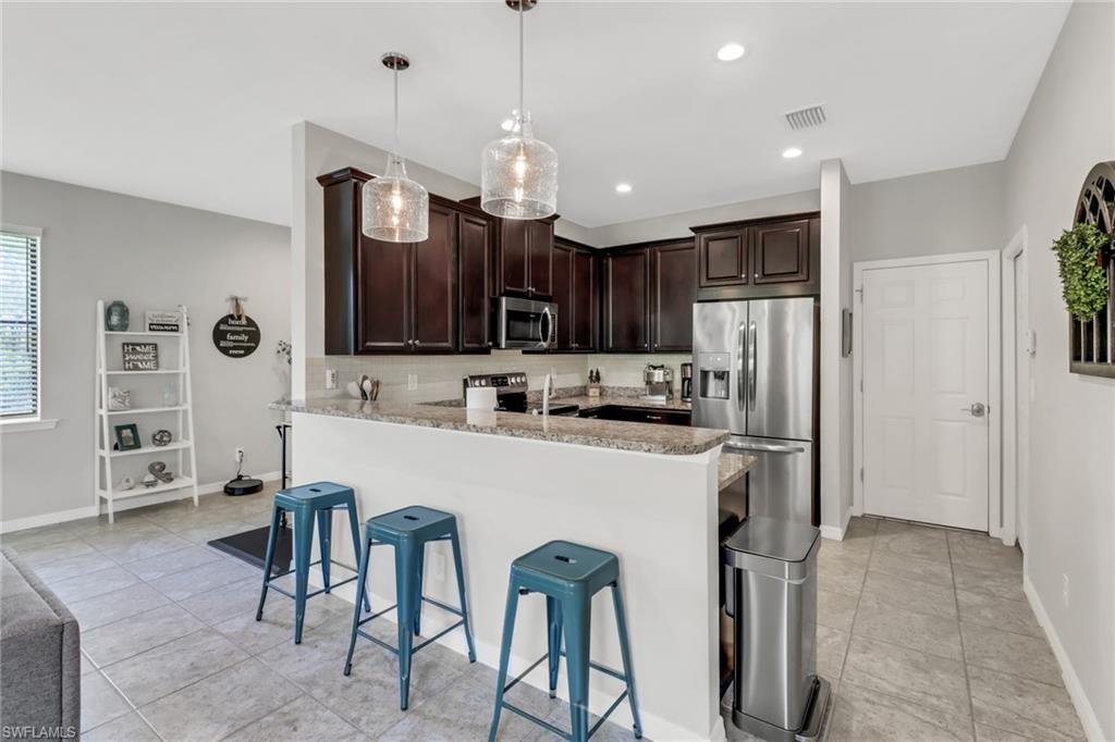 15354 Summit Pl Circle, Unit 159 Naples, FL 34119 - Photo 10 of 27 a kitchen with stainless steel appliances a refrigerator a stove a sink a center island and chairs with wooden floor