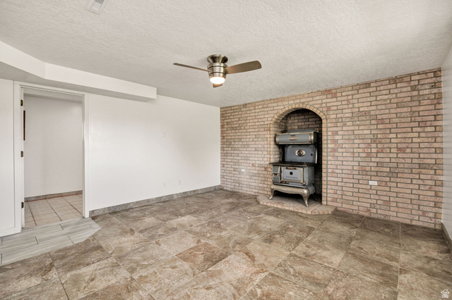 365 South Center Street Fielding, UT 84311 - Photo 21 of 41 Unfurnished living room featuring a wood stove, brick wall, ceiling fan, a textured ceiling, and stone finish flooring