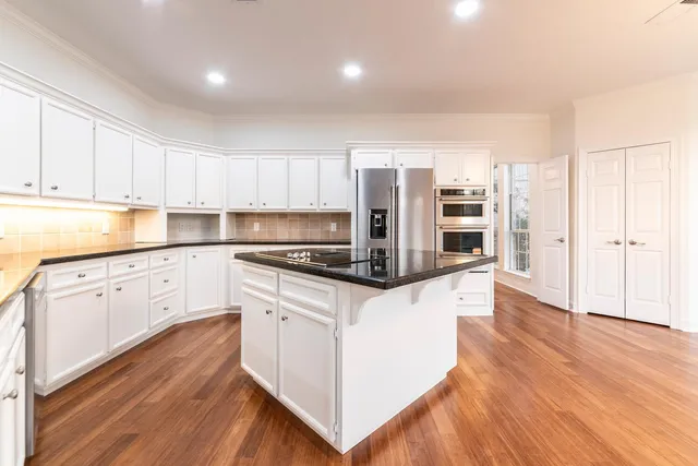 a kitchen with stainless steel appliances granite countertop a refrigerator a stove and white cabinets with wooden floor