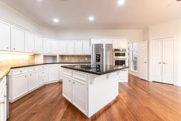 a kitchen with stainless steel appliances granite countertop a refrigerator a stove and white cabinets with wooden floor