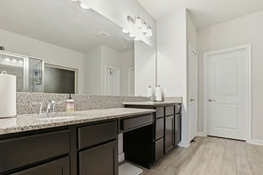 24714 Longwood Forest Drive Spring, TX 77373 - Photo 10 of 21 This bathroom features a spacious double vanity with granite countertops, sleek dark cabinetry, and modern fixtures. It includes a large mirror and a glass-enclosed shower, complemented by light-colored walls and flooring for a bright, clean look.