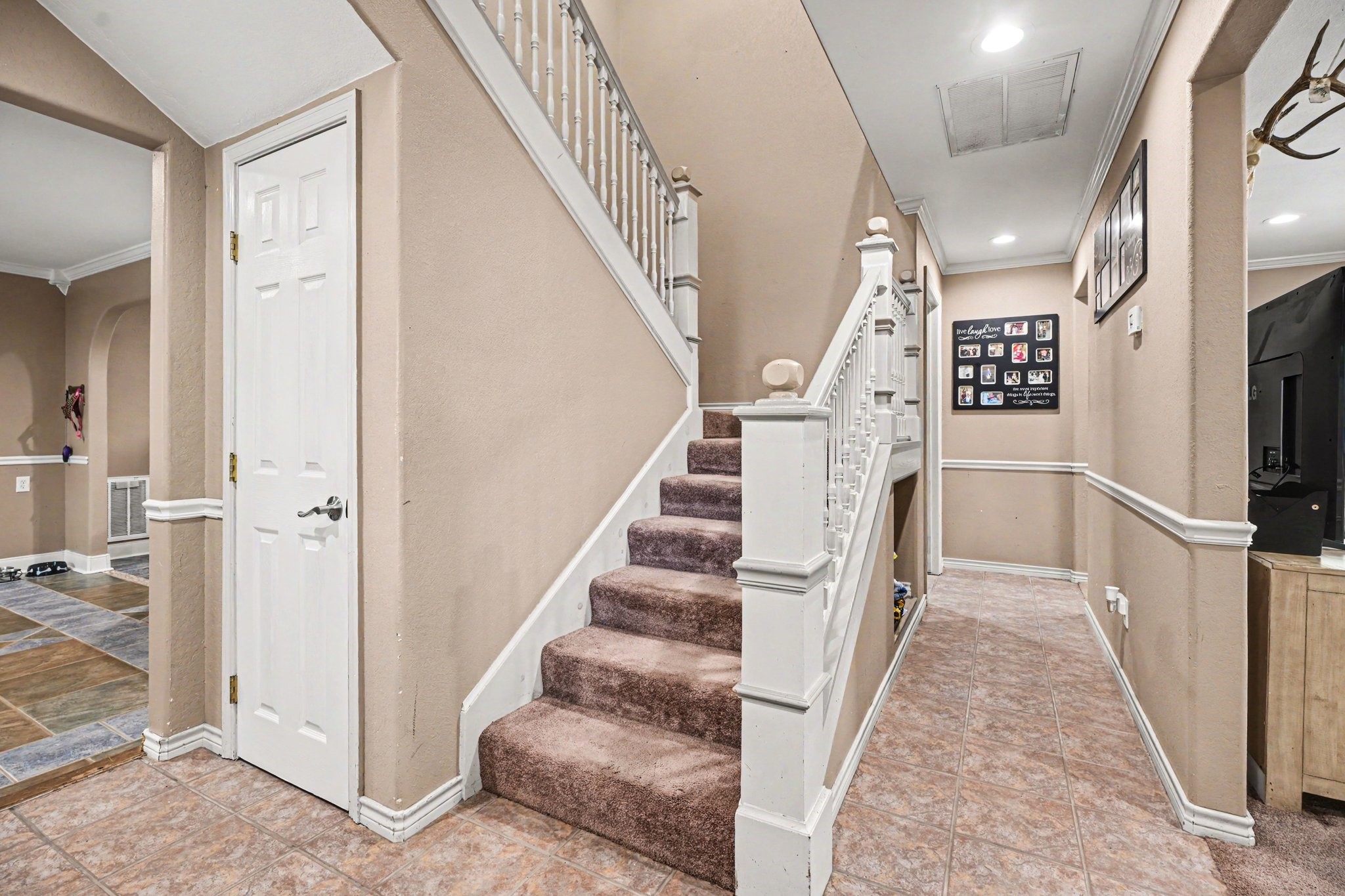 5104 Avenue R Santa Fe, TX 77510 - Photo 5 of 35 This photo shows an inviting entryway with a carpeted staircase and tiled flooring. Neutral walls feature white trim, and the area is well-lit with recessed lighting. A hallway leads to other parts of the home, enhancing the spacious feel.