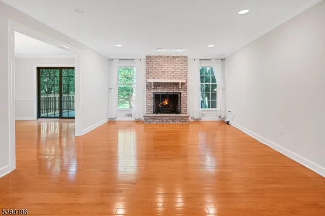 a view of an empty room with wooden floor fireplace and a window