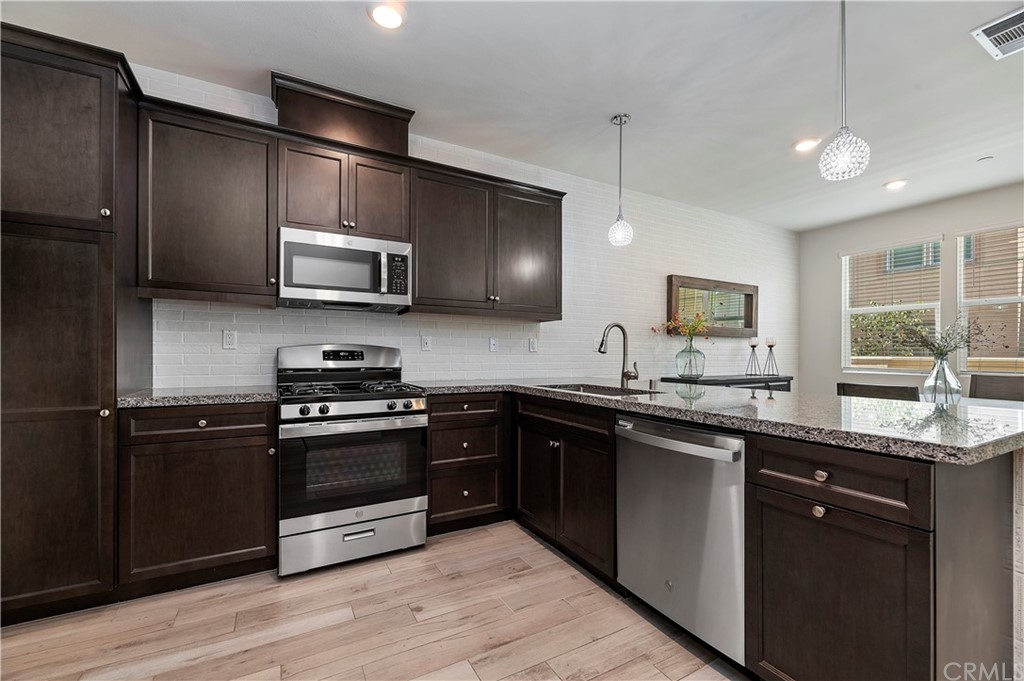 14557 Sienna Place Eastvale, CA 92880 - Photo 16 of 35 a kitchen with stainless steel appliances granite countertop a stove a sink dishwasher a refrigerator and a microwave oven with wooden floor