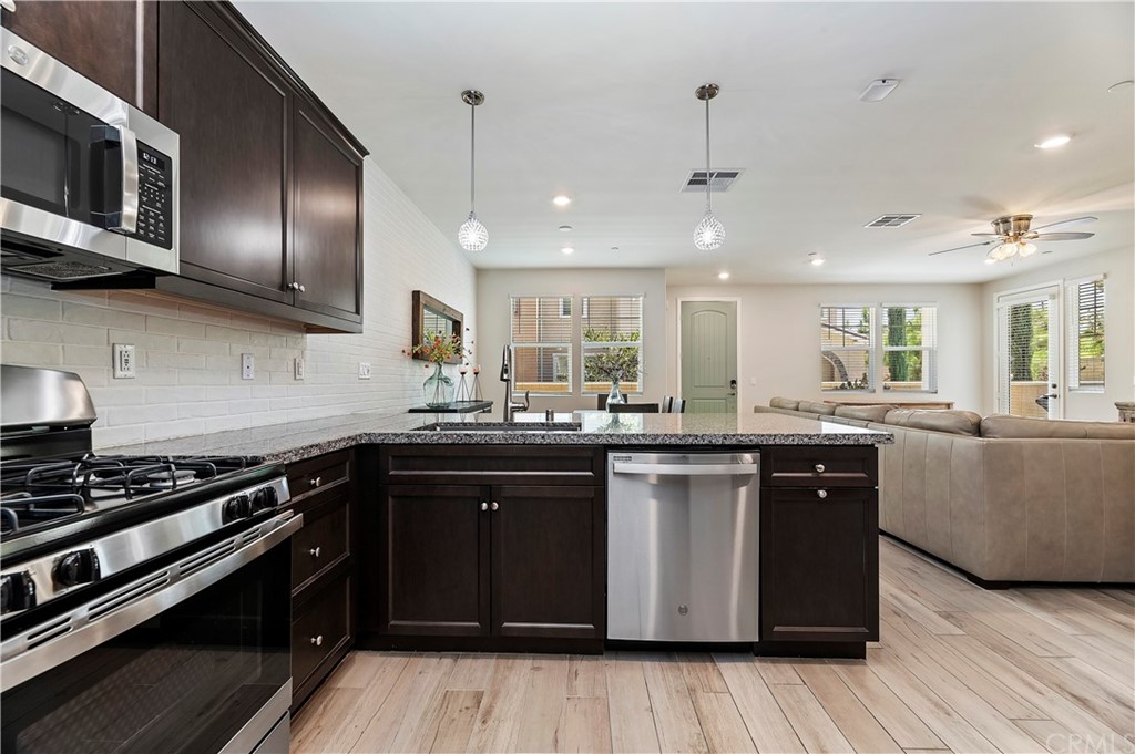 14557 Sienna Place Eastvale, CA 92880 - Photo 17 of 35 a kitchen with stainless steel appliances granite countertop wooden cabinets a stove top oven with wooden floor