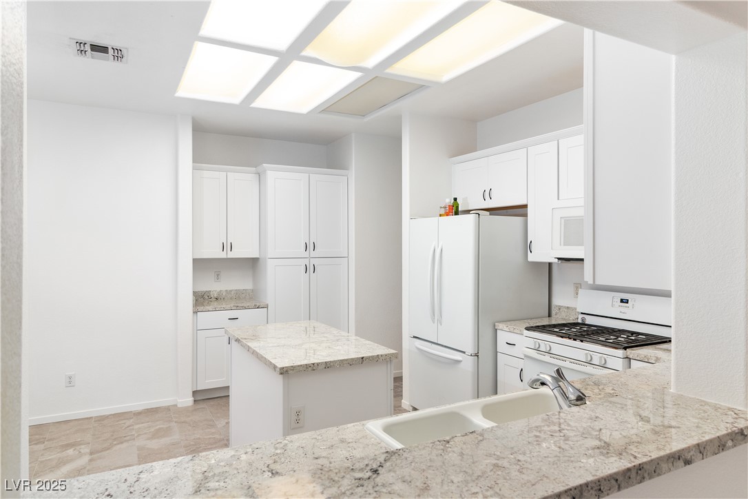 3155 Quail Song Drive Laughlin, NV 89029 - Photo 11 of 85 Kitchen with white appliances, white cabinets, granite countertops, and a kitchen island