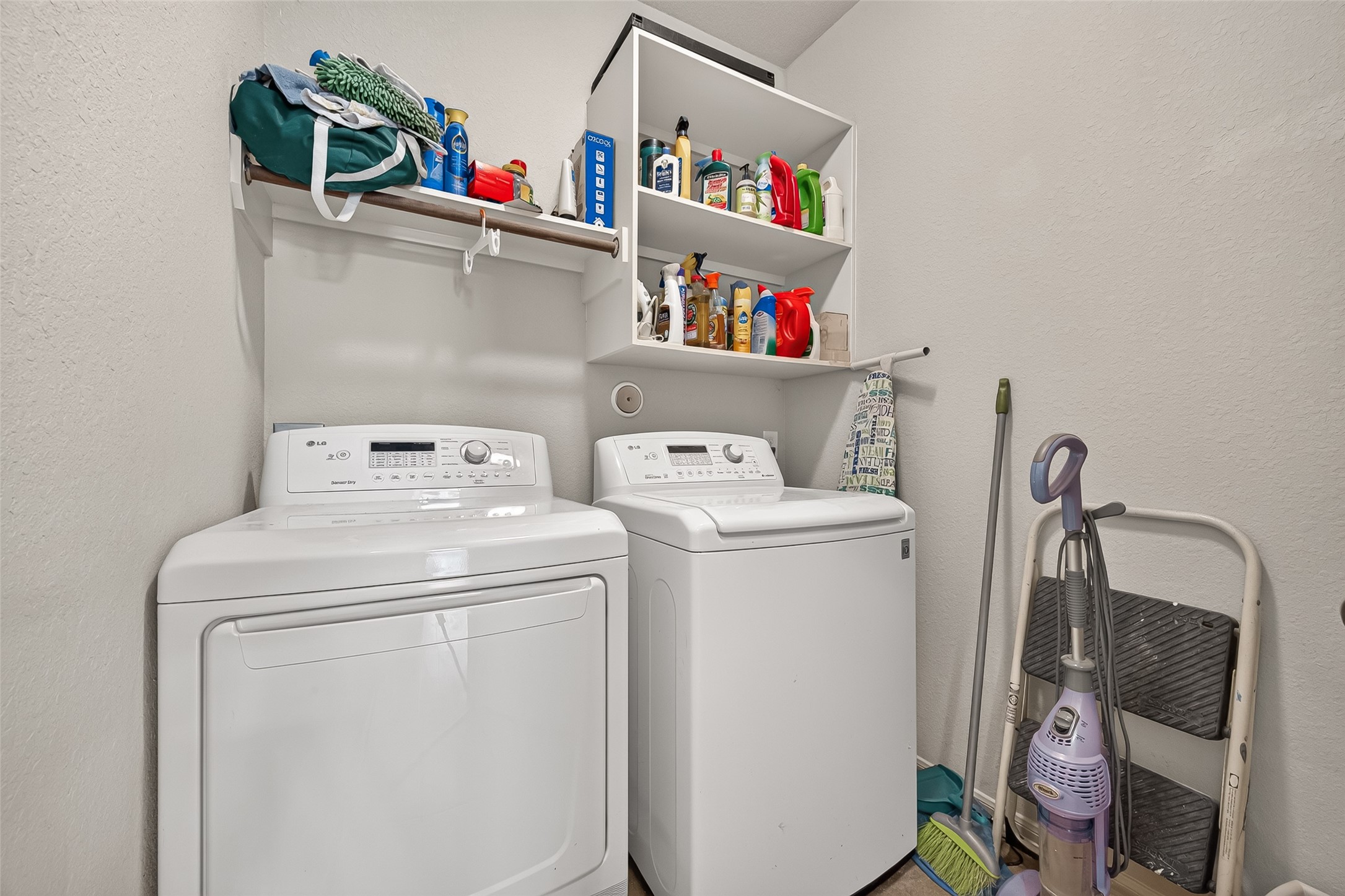 4910 Culver Lane Rosenberg, TX 77471 - Photo 40 of 50 This photo showcases the compact laundry room featuring a washer and dryer set (excluded.) It has shelving for storage of cleaning supplies and laundry essentials. The space is functional for household chores.