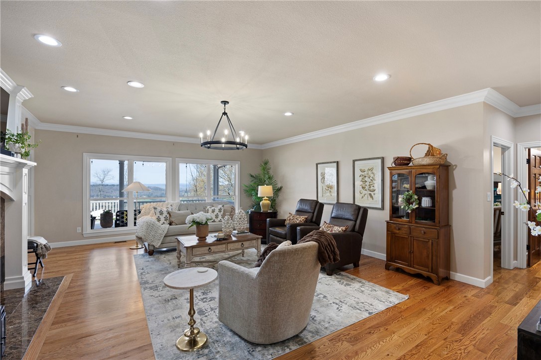 Living room with a fireplace with flush hearth, ornamental molding, light wood-style floors, and suspended lighting