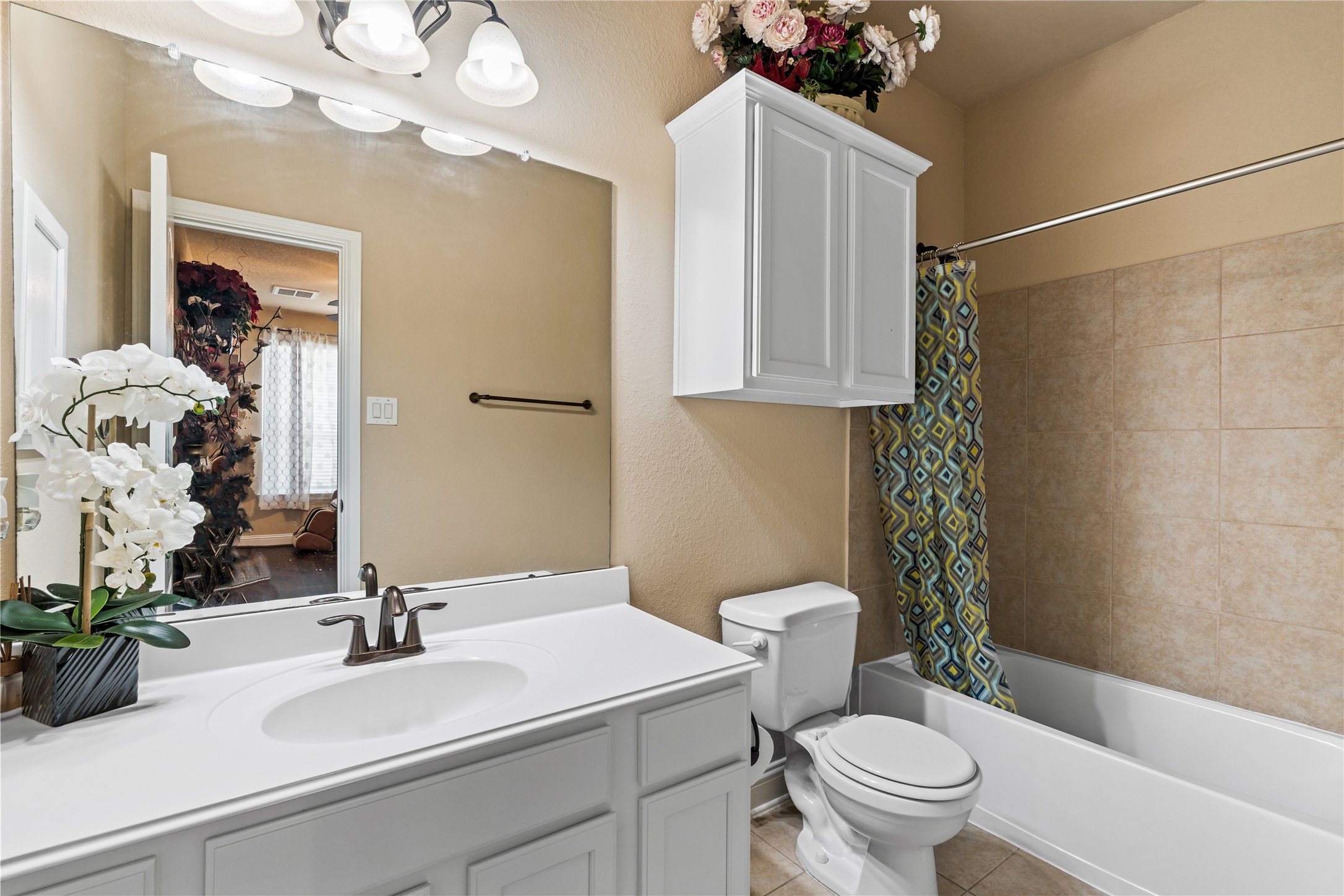5802 Layton Meadows Lane Spring, TX 77379 - Photo 27 of 42 Downstairs in law suite full bathroom. White vanity, tub/shower combo, white overhead cabinet, tile, decorative flowers. Clean and bright.