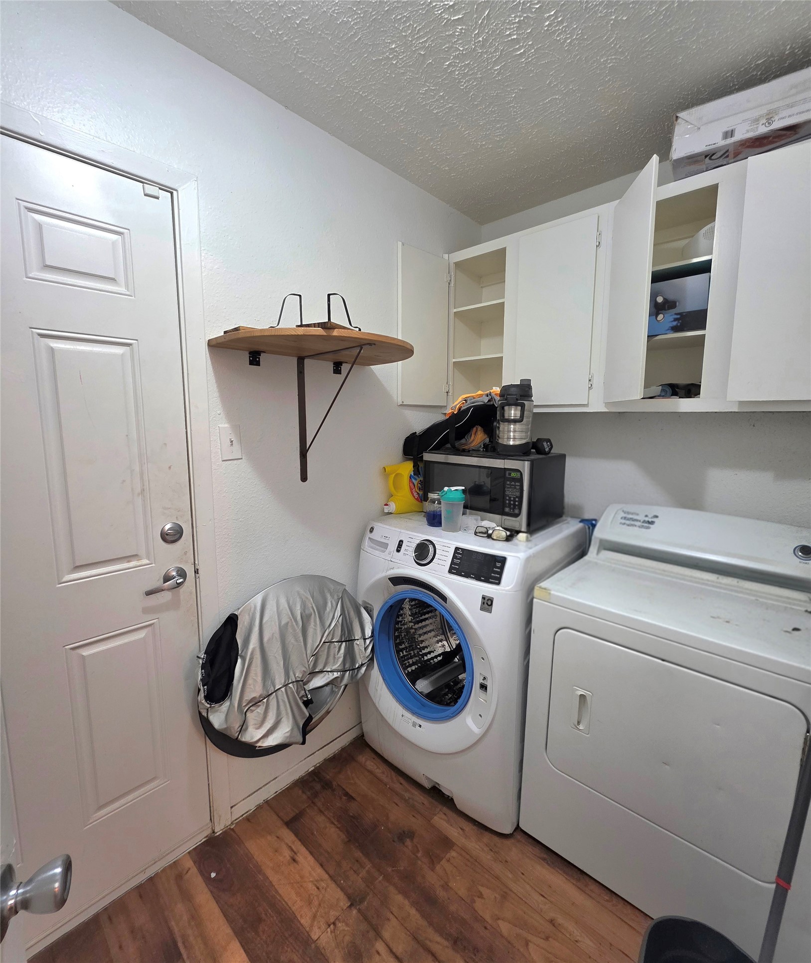 15208 Spring Hill Lane, Unit A Pflugerville, TX 78660 - Photo 11 of 16 Utility area featuring wood-finish flooring, white cabinetry, a front-loading washing machine, and a dryer