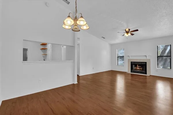 an empty room with windows fireplace and a kitchen view