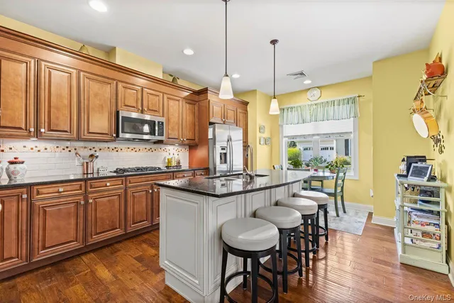 a kitchen with stainless steel appliances granite countertop a stove top oven a sink a dining table and chairs with wooden floor