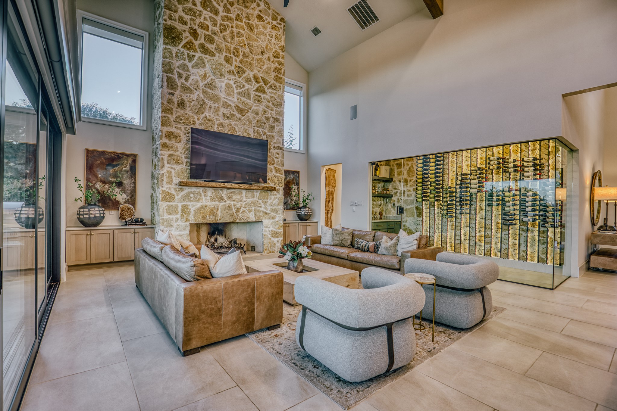 1034 Hilbun Road New Ulm, TX 78950 - Photo 20 of 49 Designed for gathering, this spectacular open-concept living space features dramatic ceiling heights, exposed timber beams, a statement stone fireplace, custom wine room, and walls of glass that open to expansive outdoor living areas.