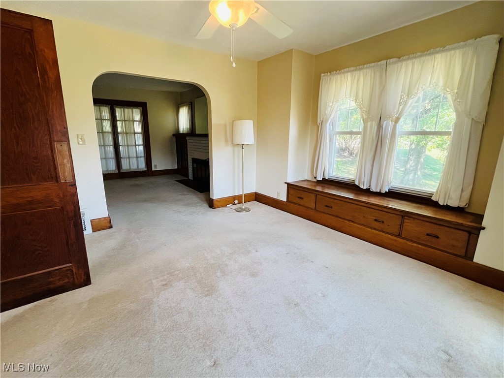 4704 South Ridge Road East Geneva, OH 44041 - Photo 20 of 49 Unfurnished room with light colored carpet, a fireplace with flush hearth, arched walkways, and ceiling fan