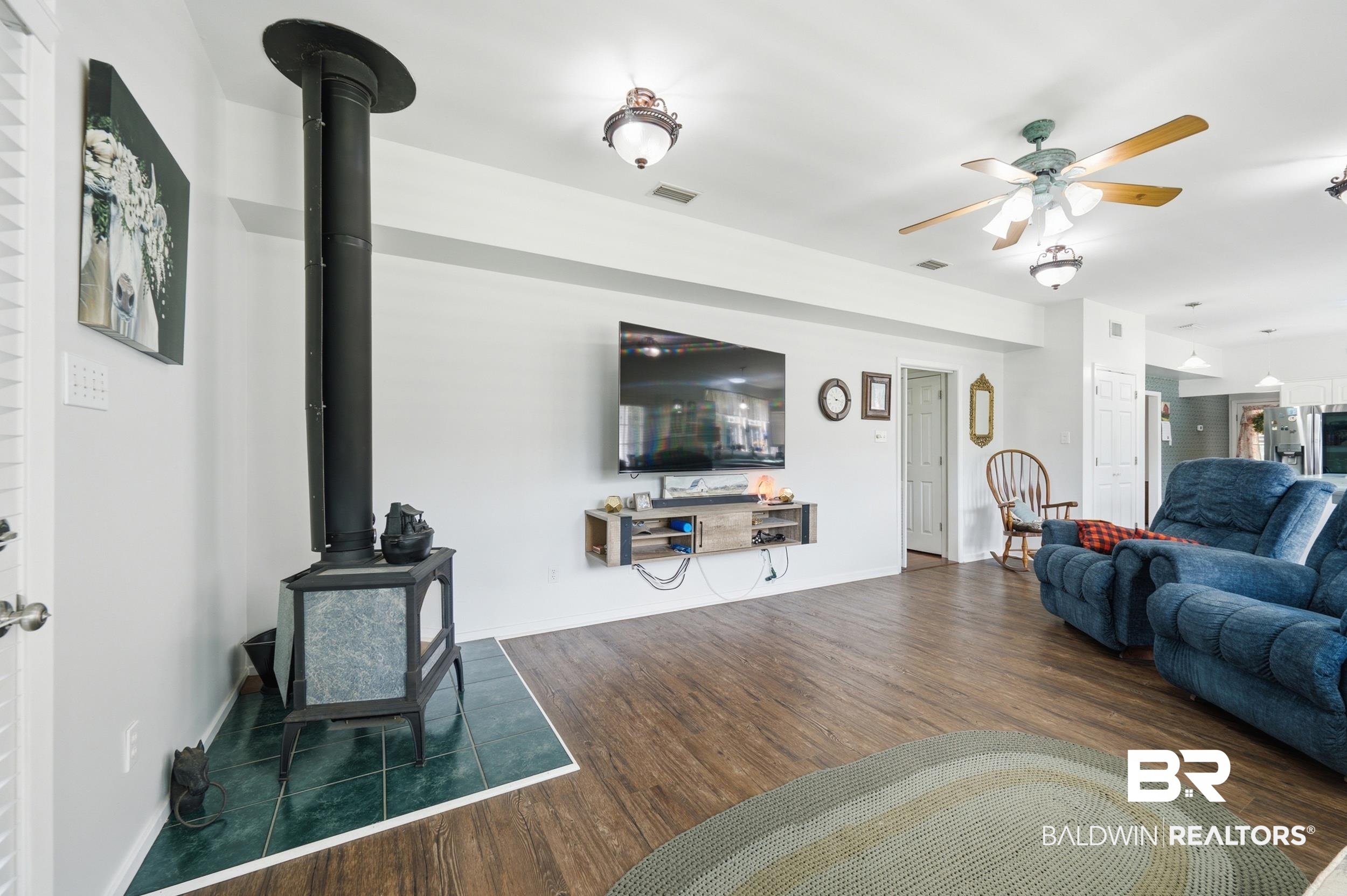 15855 Calvin Richerson Road Bay Minette, AL 36507 - Photo 35 of 83 Living area featuring wood-finish flooring, a freestanding stove with a tiled hearth, and a ceiling fan with integrated lighting