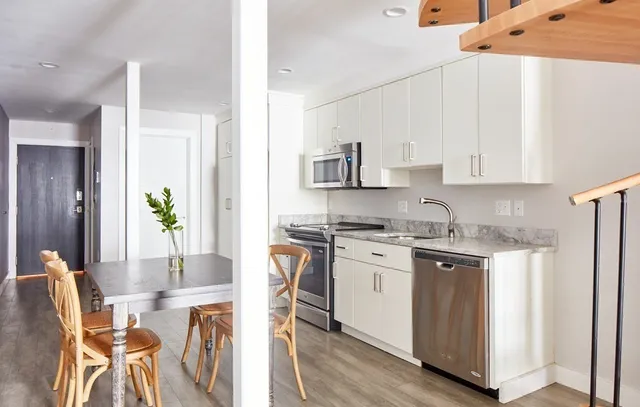 a kitchen with stainless steel appliances granite countertop a stove top oven a sink a refrigerator and white cabinets with wooden floor