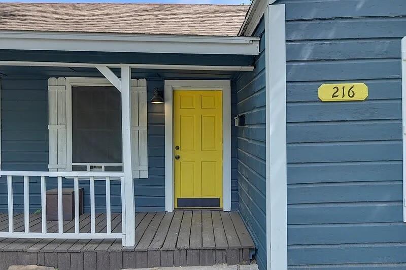 216 East Division Street Pilot Point, TX 76258 - Photo 2 of 17 Front porch entrance featuring a vibrant yellow door with a contrasting black handle, dark blue siding, and white trim