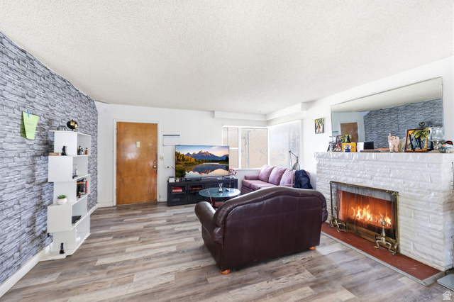 5480 South 2000th Street West Roy, UT 84067 - Photo 10 of 36 Living area with wood-finish flooring, a white-painted brick fireplace, an exposed stone-look accent wall, and a wood entry door