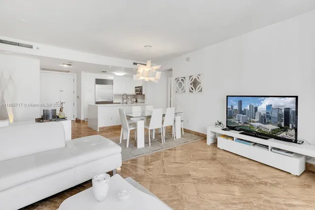 a living room with stainless steel appliances furniture a flat screen tv and a kitchen view