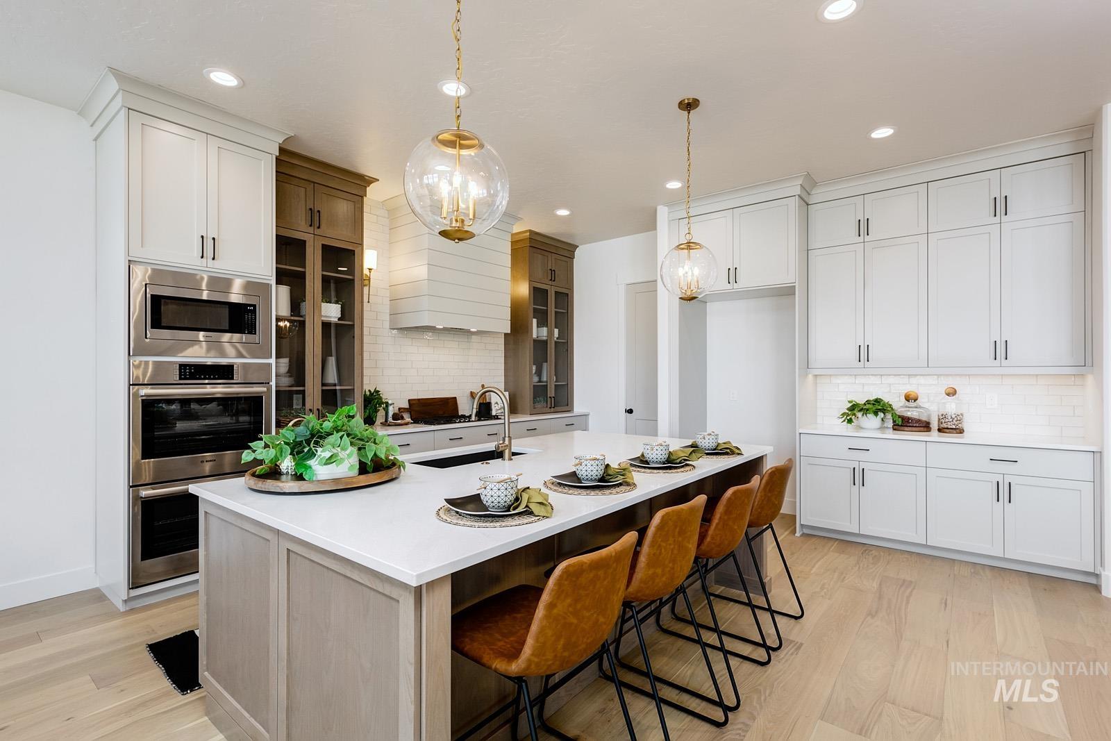 13660 North Spring Creek Way Boise, ID 83714 - Photo 10 of 42 Dual tone kitchen featuring glass insert cabinets, a breakfast bar, a kitchen island with sink, dual tone cabinetry, and stainless steel appliances