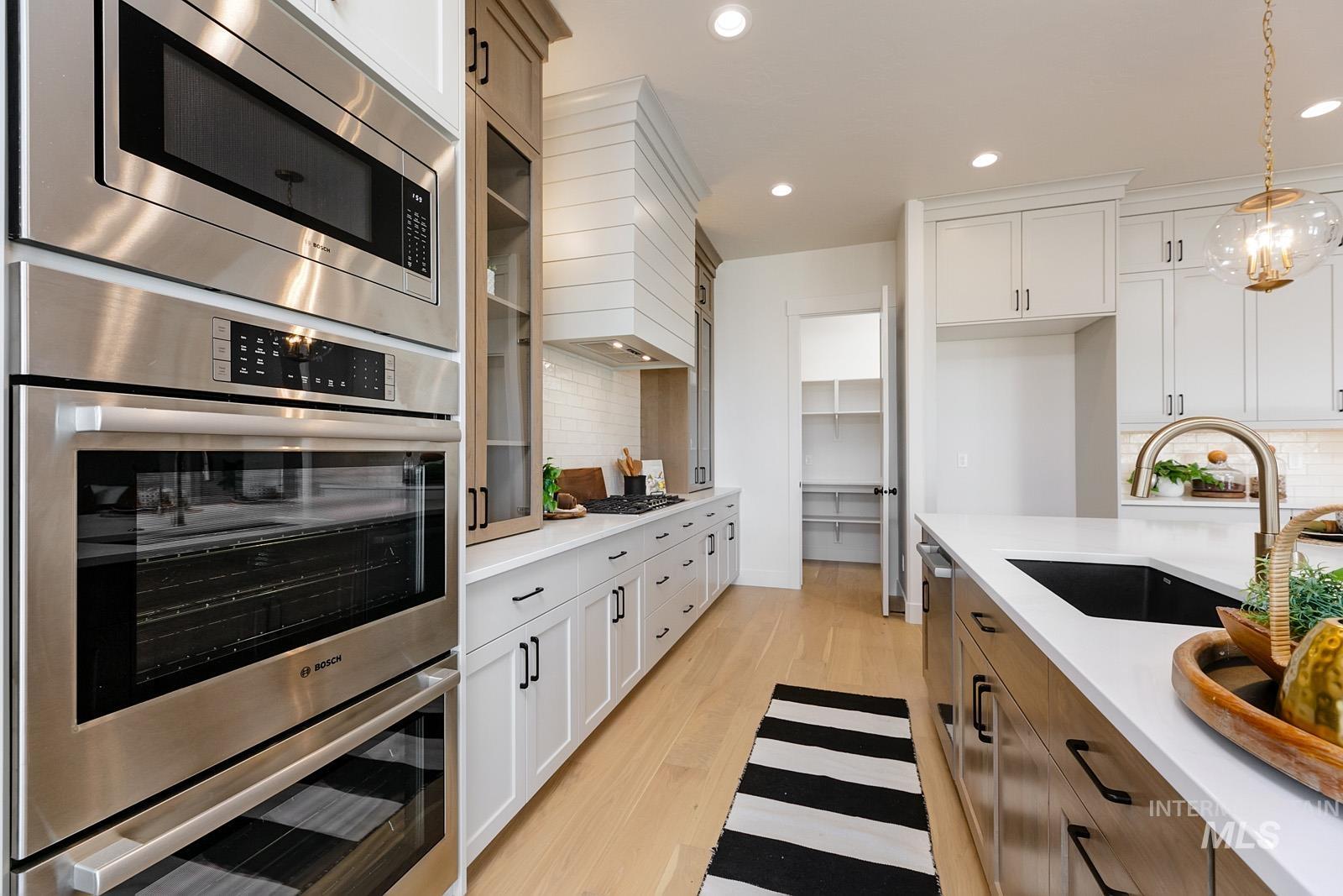 13660 North Spring Creek Way Boise, ID 83714 - Photo 11 of 42 Two tone kitchen with stainless steel appliances, hanging light fixtures, two tone color scheme, light wood-style floors, and light stone counters