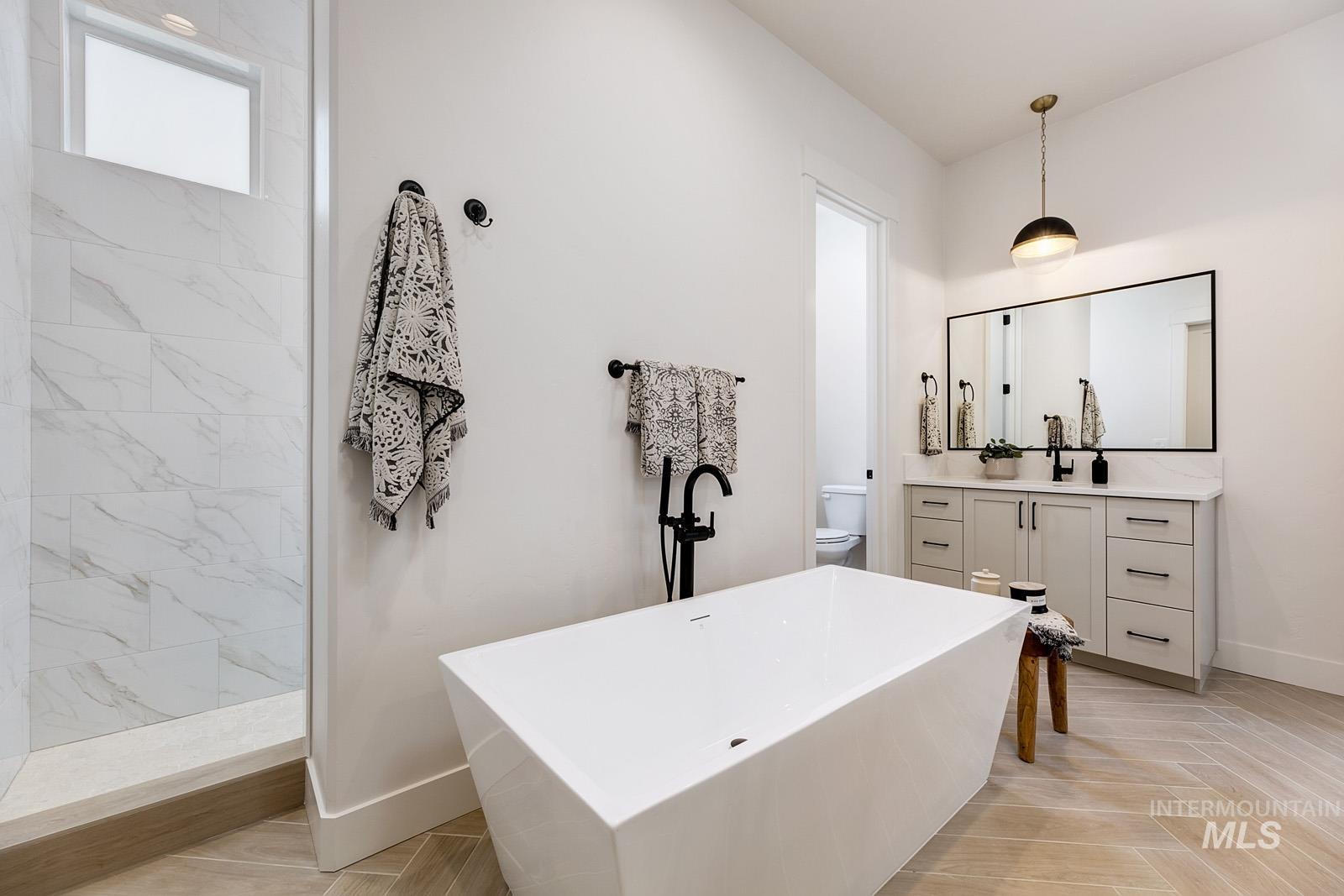 13660 North Spring Creek Way Boise, ID 83714 - Photo 15 of 42 Bathroom with vanity, a freestanding tub, a marble finish shower, and light wood-style flooring