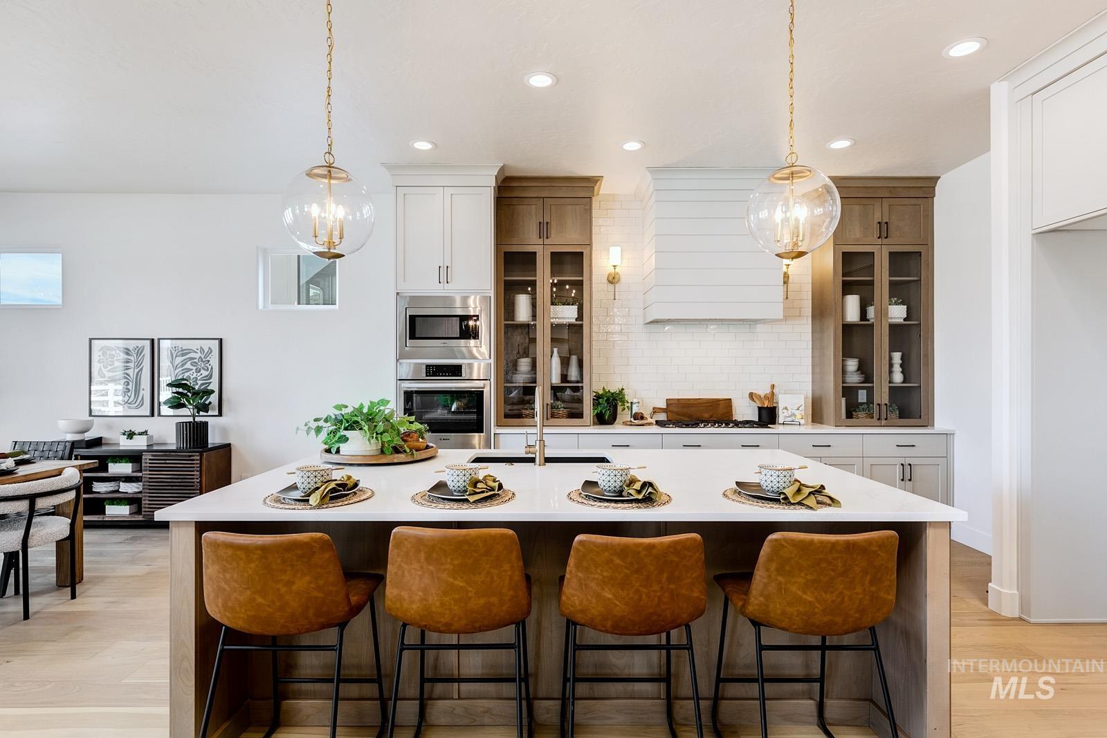 13660 North Spring Creek Way Boise, ID 83714 - Photo 6 of 42 Dual tone kitchen with a breakfast bar area, light wood-style floors, hanging light fixtures, stainless steel appliances, and a kitchen island with sink