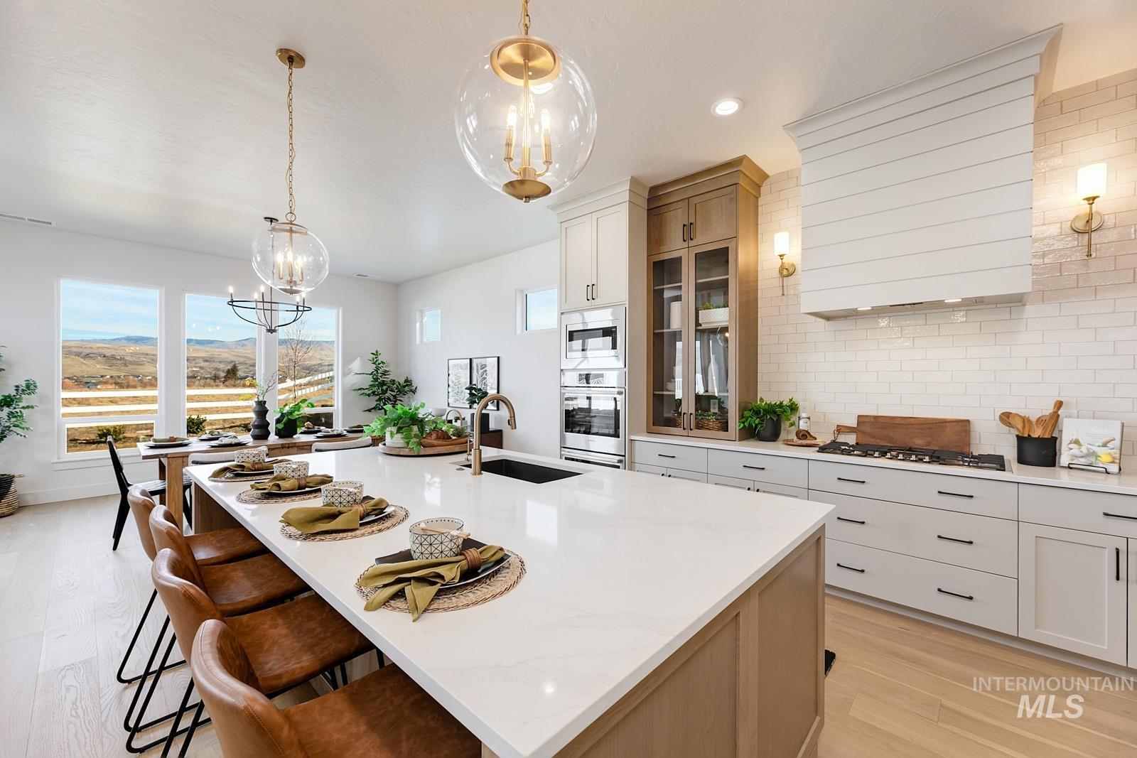 13660 North Spring Creek Way Boise, ID 83714 - Photo 7 of 42 Kitchen with two tone cabinets, hanging lights, light wood-style floors, a center island with sink, and light stone counters