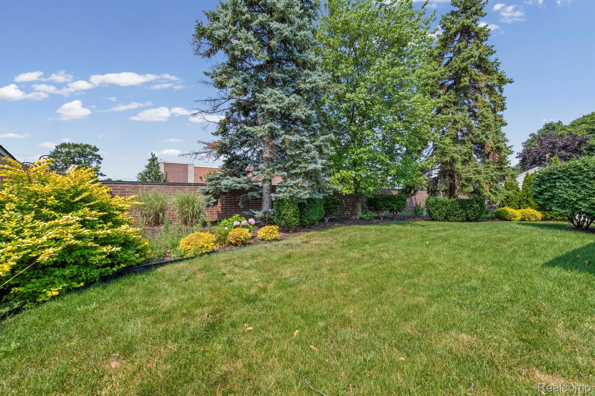 21580 Georgetown Road Trenton, MI 48183 - Photo 35 of 36 Expansive lawn area featuring mature evergreen trees, varied shrubs, and a brick privacy wall