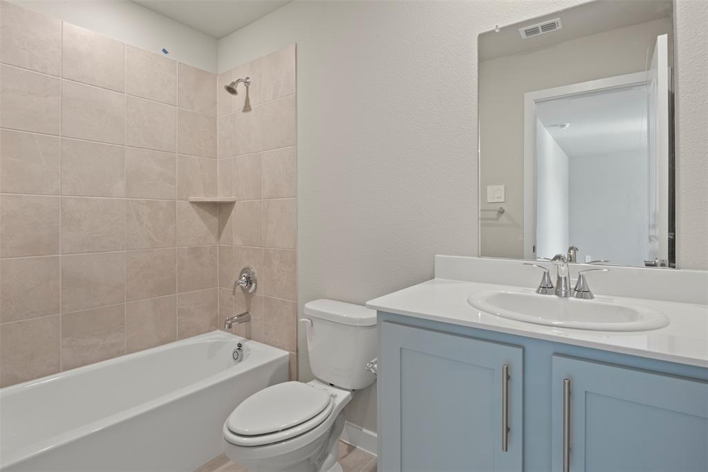 2220 Currents Road Princeton, TX 75407 - Photo 18 of 31 Bathtub with subway tile surround and built-in shelf, toilet, and vanity with light blue cabinetry and an integrated sink