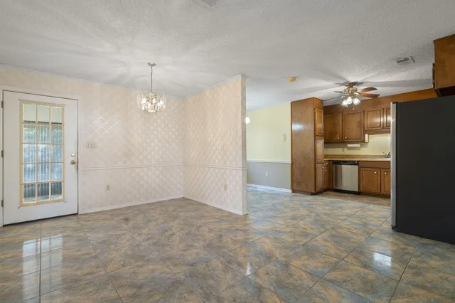 an empty room with chandelier fan and kitchen view
